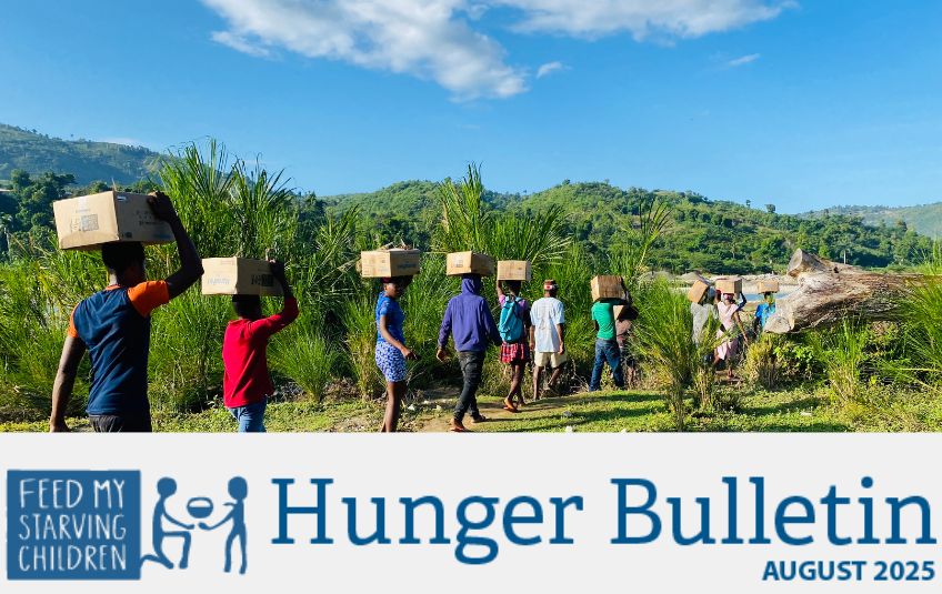 men carrying FMSC food boxes on their heads down path hunger bulletin header